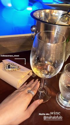 a woman's hand on a table with wine glasses, napkins and jewelry