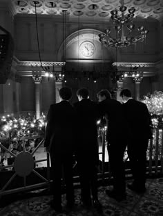 black and white photograph of three men standing in front of a large chandelier