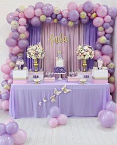 a table topped with lots of purple and white balloons next to a cake on top of a table