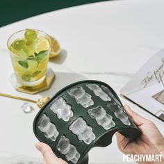 a person holding an object on top of a table next to a drink glass and book