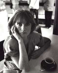 a black and white photo of a woman sitting at a table with a coffee cup