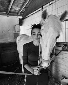 a black and white photo of a woman petting a horse's head in a barn