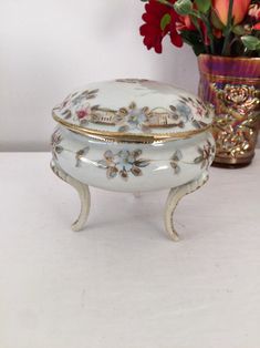 a white and gold covered box next to a vase with flowers in it on a table