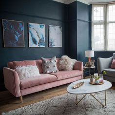 a living room with blue walls and pink couches in front of two windows,