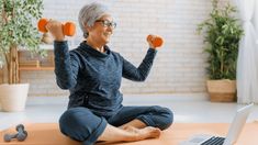 an older woman sitting on the floor with two dumbbells in front of her