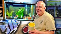 a man holding a cup next to a fish tank and an aquarium in front of him