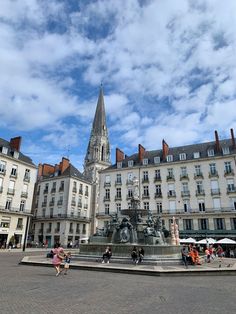 people are walking around in front of buildings and a fountain with a clock on it