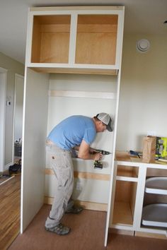 a man in blue shirt and grey pants working on a wall mounted shelf with drawers