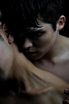 two young men embracing each other with their faces close to one another, in the dark