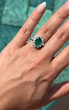 a woman's hand with an emerald and diamond ring on her finger, next to a swimming pool