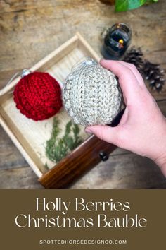 a hand holding a crocheted christmas bauble in front of a wooden box