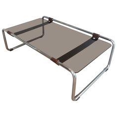 a metal and glass coffee table with two straps on the bottom, one is brown