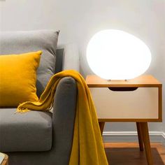 a couch with a yellow blanket on it next to a white lamp and wooden table