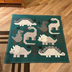 a green rug with dinosaurs on it in the middle of a wooden floor next to a dresser