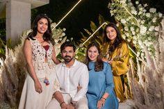 three women and one man are posing for a photo in front of a floral display