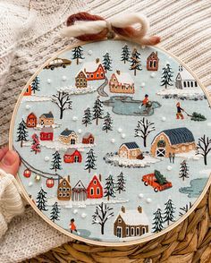 someone is holding up a hand embroidered christmas ornament with houses and trees on it