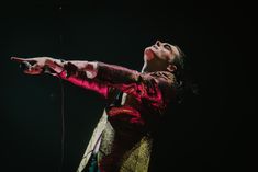 a man in red and gold outfit holding a microphone up to his mouth while standing on stage