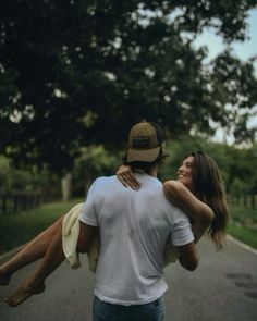 a man carrying a woman on his back while walking down the street with trees in the background