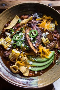 a bowl filled with meat and vegetables covered in sauce, cheese and tortilla chips