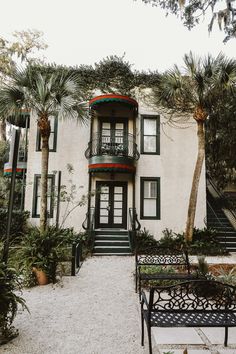 a white building with green shutters and palm trees in front of the stairs leading up to it