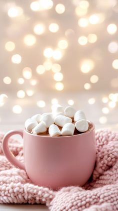 hot chocolate with marshmallows in a pink mug on a pink blanket and white lights behind it