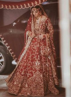 a woman in a red and gold bridal gown standing next to a white car