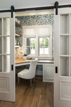 a white chair sitting in front of a window next to a wooden table and desk