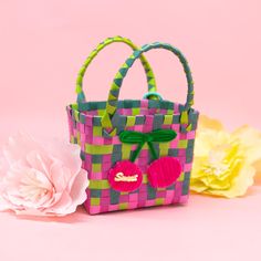 a pink and green checkered bag with pom - poms on the handles