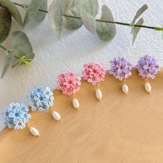 five different colors of flowers and pearls on a wooden surface next to some green leaves