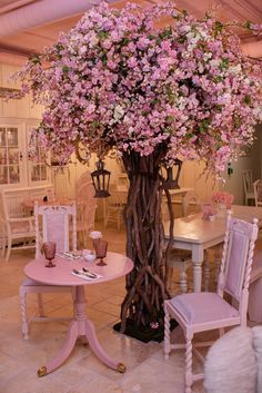 a pink table and chairs with flowers on the tree in the center is set up for a tea party