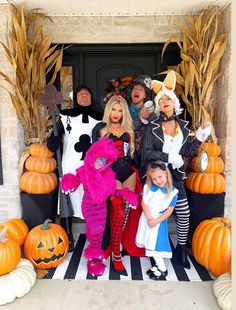 a group of people dressed up in costumes posing for a photo with pumpkins and corn stalks