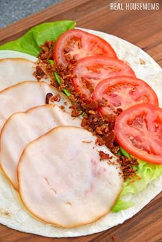 a tortilla with meat, tomatoes and lettuce sitting on a wooden table