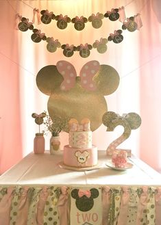 a table topped with a cake covered in pink and gold minnie mouse decorations next to a curtain