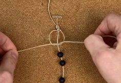 two hands are making a beaded necklace with black beads on a string that is attached to a cord