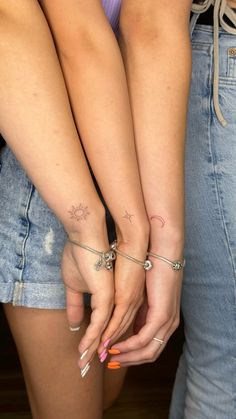 two girls with matching tattoos on their arms holding each other's hands while standing next to each other