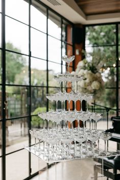 there is a very tall wine glass tower on the table in front of some windows