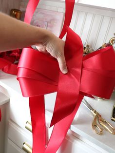 a hand is holding a red ribbon on a white counter with other items in the background