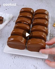 a person holding a chocolate covered doughnut in front of other desserts on a white plate