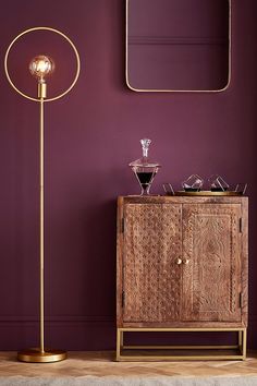 a living room with purple walls and a gold floor lamp next to a wooden cabinet