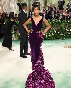 a woman in a purple gown with flowers on the side and people taking pictures behind her