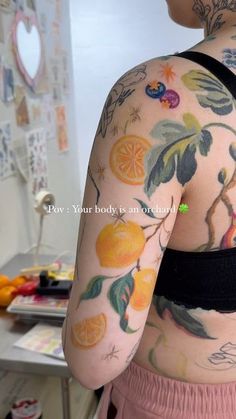 the back of a woman's body with tattoos on her arms and shoulder, holding an orange