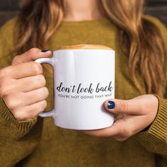 a woman holding a coffee mug with the words don't look back on it