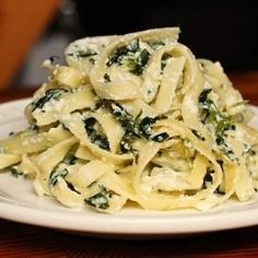 a white plate topped with pasta and spinach covered in cheese sauce on top of a wooden table