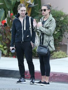 two young women standing next to each other on the street, one holding her hand