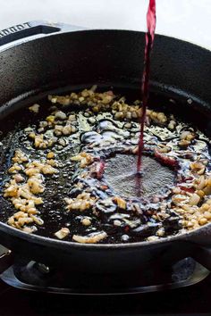 someone pouring red wine into a skillet filled with pasta and meats on the stove