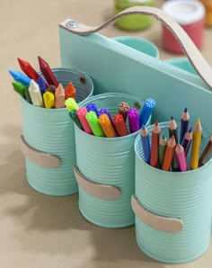 three tin cans filled with colored pencils on top of a table next to a blue case