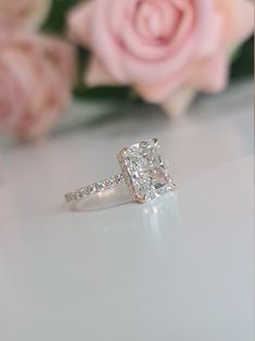 a diamond ring sitting on top of a table next to pink roses and a rose bouquet