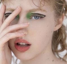 a woman with blue eyes and green make up holding her hand to her face while looking at the camera