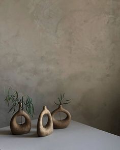 three ceramic vases with plants in them on a white table against a gray wall