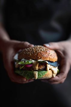 a person holding a hamburger with lettuce, onions and cheese in their hands